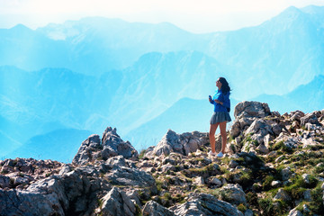 Young woman stands on the rocks and looks at the mountain.
