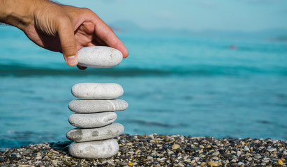 A hand constructs equilibrium on pebbles. Perfect balance of stack of pebbles on the seashore....