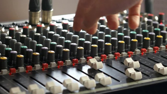 Man adjusting fader slider on audio mixer in music recording studio
