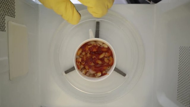 Making microwave mug lunch meal. Macaroni pasta and tomato sauce in a mug microwaving top view.