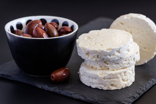 Feta cheese on black background with bowls of black olive with selective focus on cheese