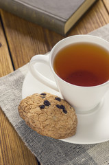 A cup of tea and some chocolate chip cookies over a books on a brown wooden table.