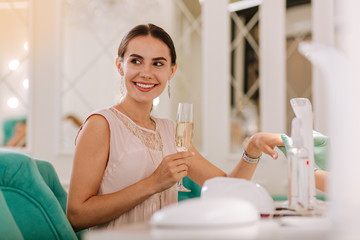 Glass of champagne. Happy beaming woman feeling carefree while holding glass of champagne visiting nail salon