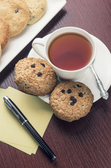 A cup of tea and some chocolate chip cookies  on a brown wooden table.