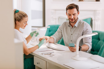 Obraz premium Sanitization of nails. Beaming attractive businessman typing message white enjoying sanitization of nails