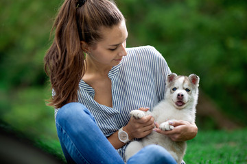 A beautiful woman with a ponytail and wearing a striped shirt is holding a sweet husky puppy on the lawn. Love and care for pets.