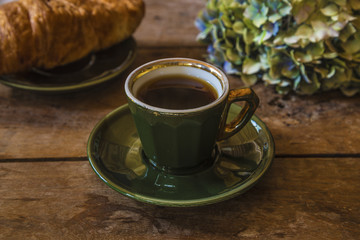 French breakfast in retro style: espresso in retro cup of parisian bistrot, croissant and hydrangea flower on old wooden background