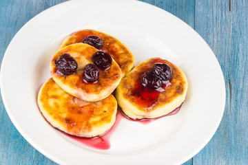 Russian cheesecakes with cherry jam on a white plate