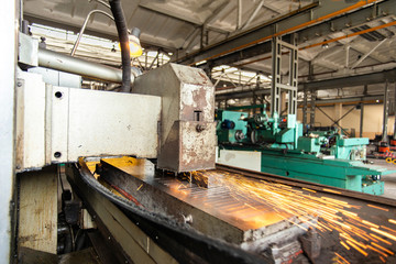 Metal parts on a flat grinder are treated with an abrasive wheel, sparks fly from under the circle, wide-angle photos.