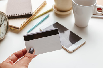 Woman holding credit card over white office desk with smartphone