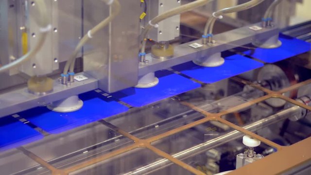 Industrial machine takes solar cells from a stencil plate and putting them on the conveyor belt