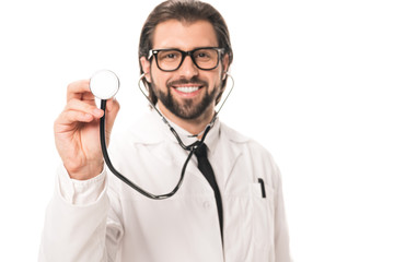 happy bearded doctor in white coat and eyeglasses holding stethoscope and smiling at camera isolated on white