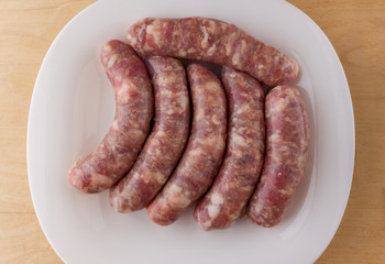 Raw sausages for a barbecue on a white plate. Several barbecue sausages lie next to each other.