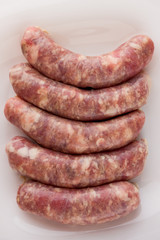 Raw sausages for a barbecue on a white plate. Several barbecue sausages lie next to each other.