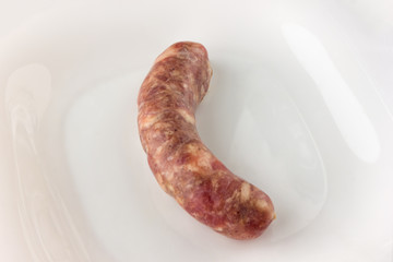 One raw sausage for a barbecue on a white plate. sausage close-up on a white surface.