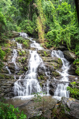 Fototapeta na wymiar Beautiful large waterfall flowing between rocks in a deep green forest. Waterfall flowing over rocks. Nature background.