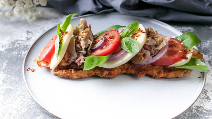 Mediterranean Kitchen. Sandwich with smoked chicken, mozzarella, tomatoes, sweet onions and basil leaves on a round plate on a concrete background. Close-Up