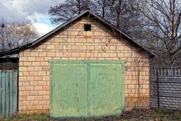 old brick garage with green brick gate and part on the street in the grass