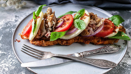 Delicious Italian sandwich with smoked chicken, mozzarella, tomatoes, sweet onions and basil leaves on a round plate on a concrete background. Close-Up