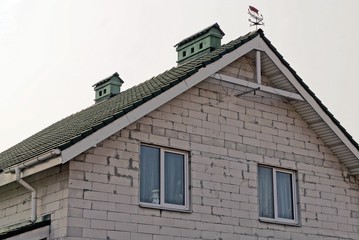 part of a gray brick house with windows under a green tiled roof