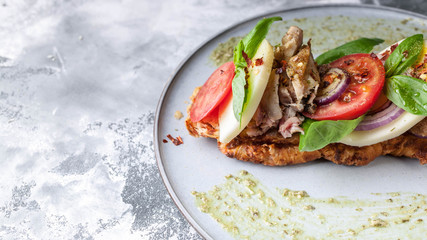 Italian sandwich with smoked chicken, mozzarella, tomatoes, sweet onions, basil leaves and pesto sauce on a round plate on a concrete background. Mediterranean Kitchen. Close-Up