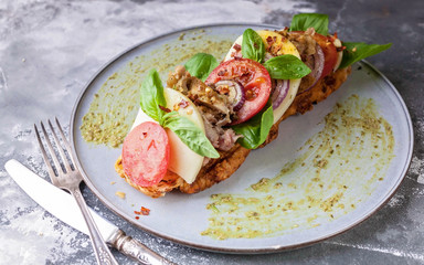 Italian sandwich with smoked chicken, mozzarella, tomatoes, sweet onions, basil leaves and pesto sauce on a round plate on a concrete background. Mediterranean Kitchen. Close-Up