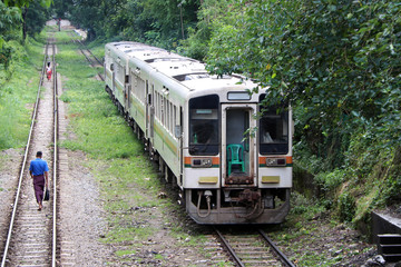Naklejka premium Pociąg jedzie po torze. za wieśniakiem Myanmarese idącym równoległym torem kolejowym.