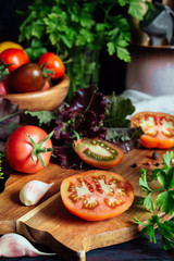 Fresh tomatoes and parsley, dill, garlic on a dark background in a rustic kitchen and wooden utensils still life with copy space