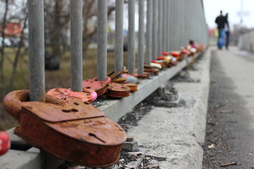 Rusty lock on the railing of the grey bridge in perspective with a blurred couple of people leaving...