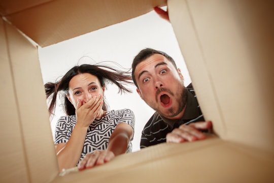 The surprised man and woman unpacking, opening carton box and looking inside. The package, delivery, surprise, gift and lifestyle concept