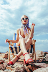 bottom view of elegant attractive girl in retro swimsuit sitting in beach chair