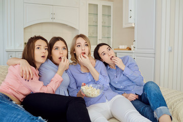 Young girls watching TV, eating popcorn sitting on the couch in the room.