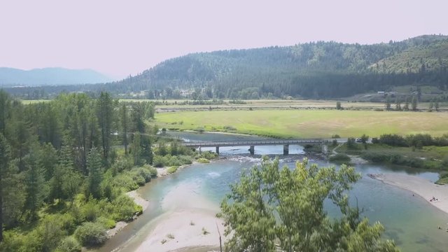 Aerial View Over Tree in Middle of River Panning Down Focusing on Small Bridge Over River - Priest River Idaho