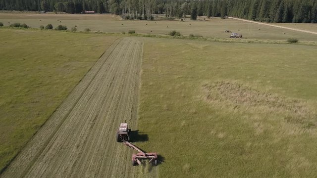 Aerial View of Small Farm Tractor Cutting Hay Field Passing Over Equipment