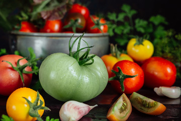 Fresh tomatoes and parsley, dill, garlic on a dark background in a rustic kitchen and wooden utensils still life with copy space