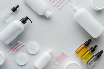 top view of bottles of cream, natural oils and cotton swabs on white tabletop, beauty concept