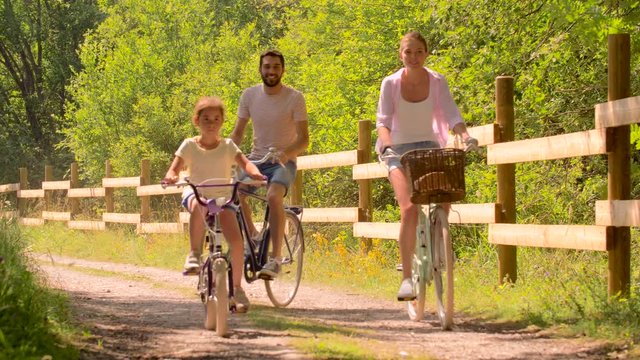 family, leisure and people concept - happy mother, father and little daughter riding bicycles in summer park