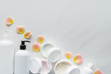 top view of bottles of cream and rose petals on white tabletop, beauty concept
