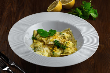Tasty ravioli stuffed with ricotta, mint and grated lemon ring in a soup plate. First class Italian pasta food on a brown wooden table.