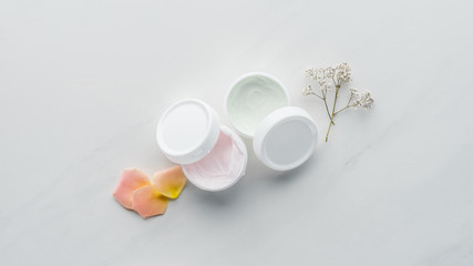 top view of bottles of cream, dried flowers and rose petals on white surface, beauty concept