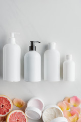 top view of bottles of cream, pieces of grapefruit and rose petals on white surface, beauty concept