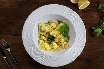 Gourmet Italian ravioli made of pasta dough, ricotta, mint and grated lemon served in a soup plate on a dark brown wooden table. Top view.