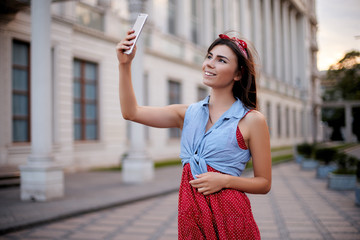 Portrait of wonderful caucasian woman taking selfie with smartphone in Europe. Brunette female hipster with piercing in nose making self portrait with cellphone camera on european street on vacation.