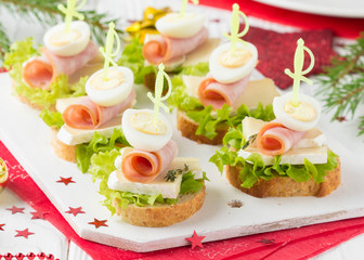 Christmas canapes on bread with brie or Camembert cheese, ham and boiled quail egg. Beautiful presentation on the festive new year's table. Delicious starter
