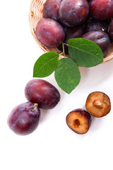 Yellow wooden basket with ripe plums, whole and half ripe plums isolated on a white background..