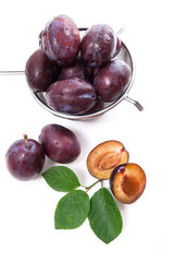 Steel colander with ripe plums, whole and half ripe plums with leaf isolated on a white background..