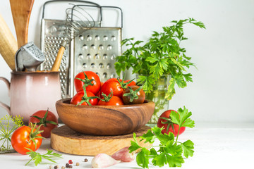 Fresh tomatoes and parsley, dill, garlic on a light background in a rustic kitchen and wooden utensils still life with a copy space