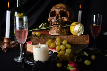 Naturaleza muerta con una calavera con rosas, libros, frutas, vino y velas sobre un fondo oscuro