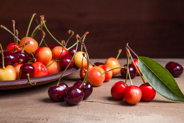 Clay plate with yellow and red sweet cherry on wooden background.