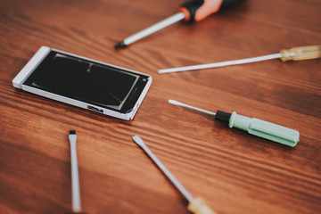 Broken Mobile Phone with Tools on Wooden Table.